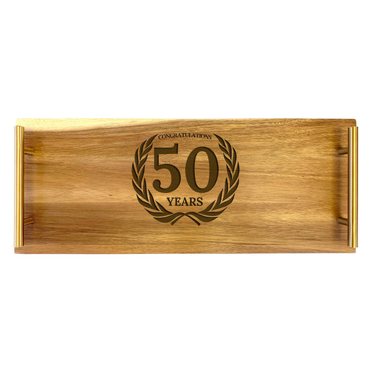 A large wooden serving tray with a gold-colored engraved message 'CONGRATULATIONS ON YOUR 50TH ANNIVERSARY' surrounded by a laurel wreath.