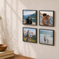 Four square framed photo tiles with black frames arranged in a 2x2 grid on a beige wall, styled in a warm home interior with a wooden bowl, books, and a potted plant nearby.